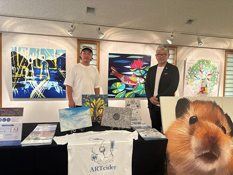 写真左から アヒ氏、山西氏 ファブリックボード展示作品の前で